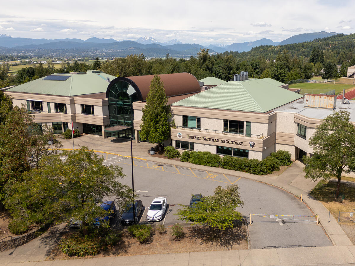 Exterior image of a secondary school. It is of the front of the building where the entrance is. Mountain range in the far back distance along with some green landscape in behind the school building.