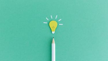 Creative composition of pencil with small paper light bulb glowing above on green background