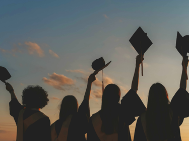 students in caps & gowns holding up their caps